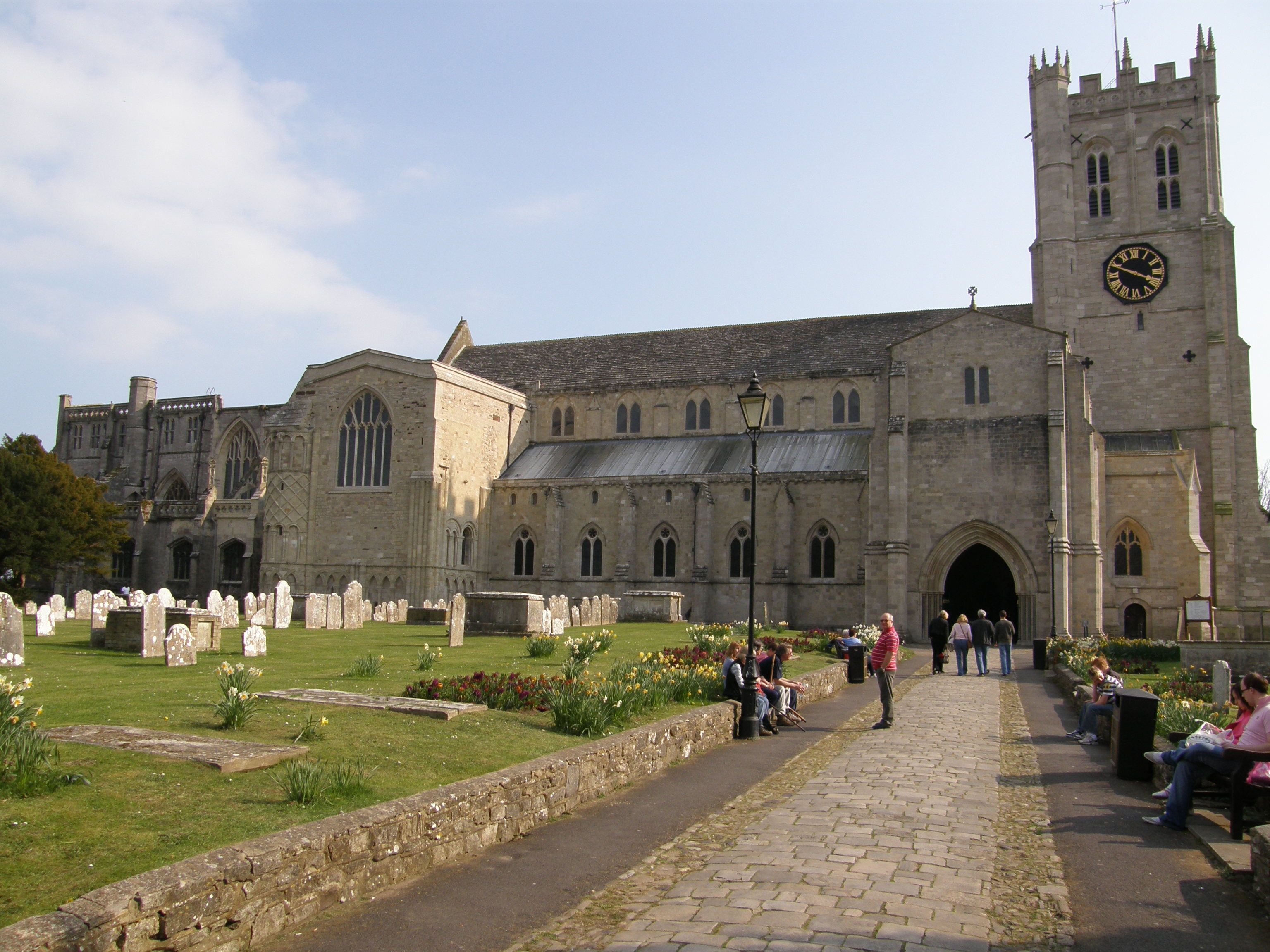 A historic church with a large clock tower, a cemetery in front, and a cobblestone pathway.