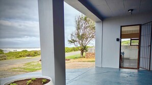 Un espace extérieur abrité, doté d’un sol en béton, d’un bac à fleurs blanc contenant des plantes et offrant une vue sur une route et la verdure environnante.