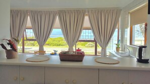 Une cuisine avec vue sur la mer, un évier, une bouilloire et un panier posé sur le plan de travail.