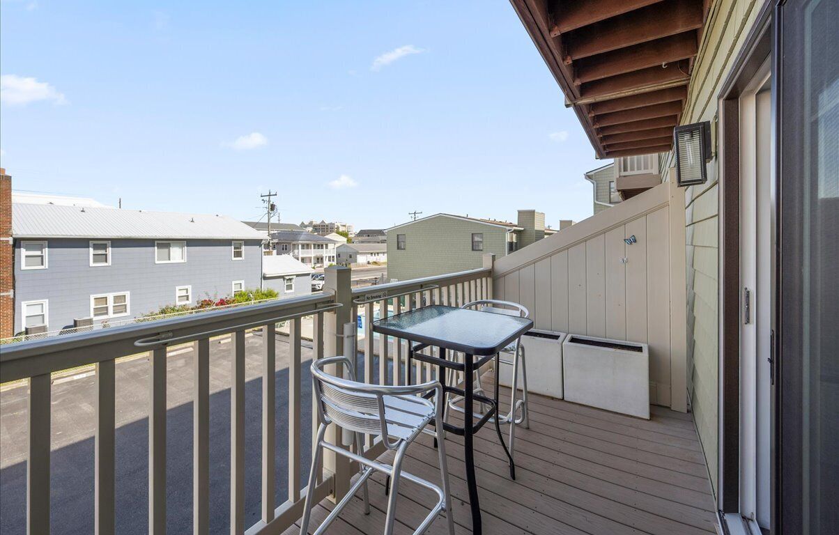 A balcony with a table and chairs, a view of neighboring buildings, and a wooden deck.