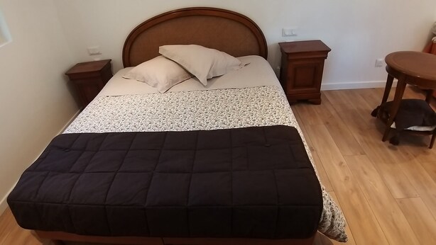 Une chambre à coucher comprenant un lit, deux tables de chevet, une tête de lit en bois, une fenêtre et une petite table ronde.
