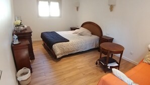 Une chambre à coucher avec un lit, une commode, une table de chevet, une petite table et une fenêtre.