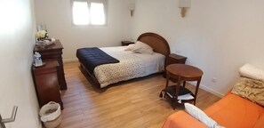 Une chambre à coucher avec un lit, une commode, une table de chevet, une petite table et une fenêtre.