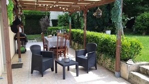 Une terrasse extérieure agrémentée d’une pergola, d’une table dressée pour le repas et de chaises en osier.