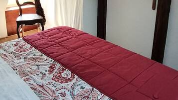 Une pièce comprenant un lit, une chaise, une porte avec des crochets et une fenêtre avec des rideaux.
