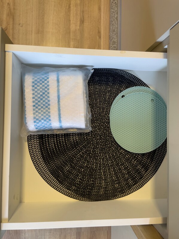 Un cajón con un tapete negro tejido, una toalla azul y blanca a cuadros y un tapete verde circular.
