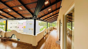 A covered outdoor area with a wooden ceiling, a seating area with chairs, and a view of buildings in the background. - Millennium Eco Retreat (Coimbatore)