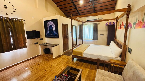 A four-poster bed with a wooden frame, a television mounted on the wall, a painting of a moon, and a window with curtains. - Millennium Eco Retreat (Coimbatore)