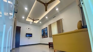 A spacious living room with a ceiling fan, a clock, a television, and a sofa. - Millennium Eco Retreat (Coimbatore)