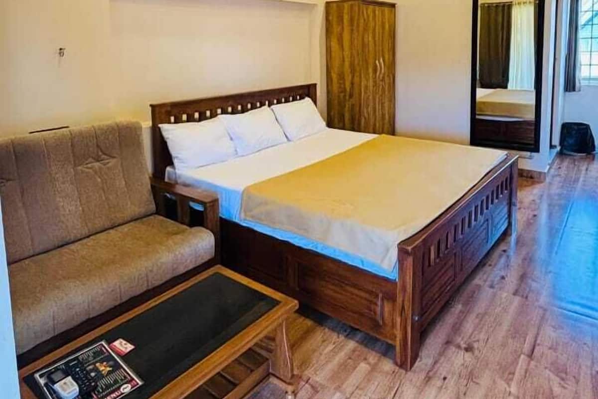 A bedroom with a bed, a sofa, a wooden coffee table, and a ceiling fan.