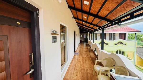 A corridor with a wooden floor, a door with a brass handle, and a balcony with wicker chairs.