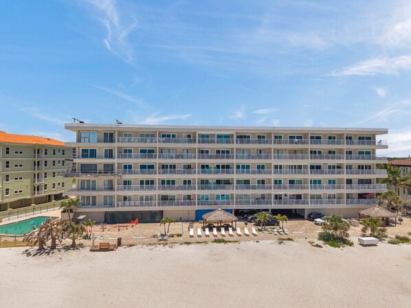A multi-story hotel with balconies, a pool, and beachside amenities. - Beachfront End Unit 3-Bedroom with Wrap-Around Balcony (Indian Shores)