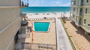 A pool area with a clear view of the ocean, a fenced swimming area, and a building with balconies. - Beachfront End Unit 3-Bedroom with Wrap-Around Balcony (Indian Shores)