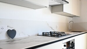 Eine moderne Küche mit Marmorarbeitsplatte, einem Gasherd, einem Geschirrspüler und einer herzförmigen Dekoration an der Wand.