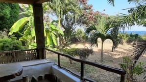 A covered outdoor seating area with a view of a garden and the sea. - Mango Lodge Msambweni (Msambweni)
