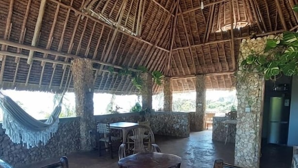 A thatched-roof outdoor seating area with wicker furniture and a stone wall backdrop. - Mango Lodge Msambweni (Msambweni)