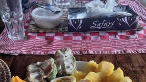 A dining table with a checkered tablecloth, a plate of assorted fruits, a box of facial tissues, and a thermos. - Mango Lodge Msambweni (Msambweni)