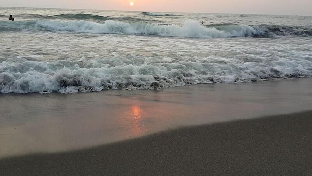 Een strand met golven en een ondergaande zon op de achtergrond.