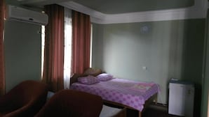 Een kleine, eenvoudige kamer met een bed, twee stoelen, een verwarming en een koelkast.