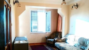 Een woonkamer met een bank, een stoel, een tafeltje en een raam met jaloezieën.