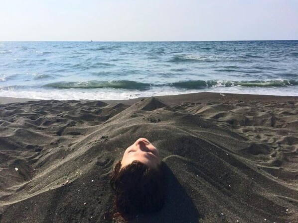 A person lying on a sandy beach with the ocean in the background. - Hotel Shorena Ureki (Ureki)