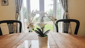 Una mesa de comedor con una orquídea blanca en una maceta blanca, dos sillas y un cuadro en la pared.