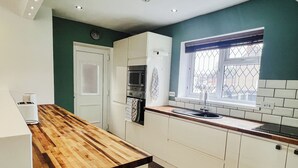 Una cocina con mostradores de madera, armarios blancos, horno empotrado y una ventana con reja de metal.