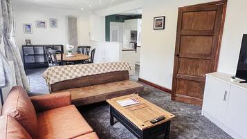 A living room with a brown sofa, a wooden coffee table, and a kitchen area in the background.