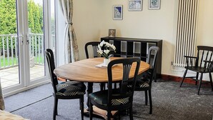 Un comedor con una mesa redonda, sillas negras y un aparador tipo buffet. Hay tres luces en el techo, un radiador y una ventana con cortinas.