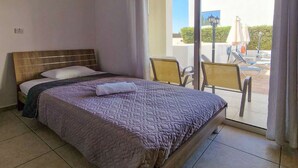 Una camera d'albergo con un letto, un balcone con sedie e un ombrellone, e vista all'esterno.