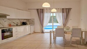 Una cucina moderna con mobili bianchi, una parete di sfondo in marmo e un'area pranzo con tavolo e sedie.