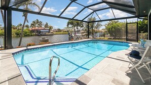 Piscina con vista a un lago y palmeras, rodeada por un porche cubierto con sillones de descanso.