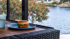 Una mesa con un plato de comida y una bebida, con vista a un cuerpo de agua y una casa.