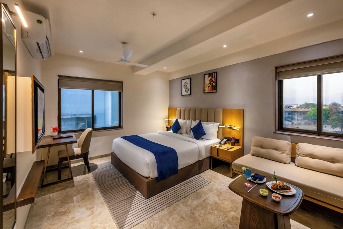 A modern hotel room with a large bed, a desk, a sofa, and a view of the city.