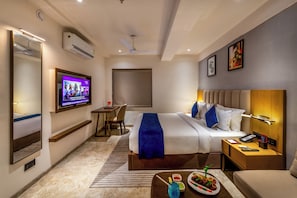 Ein Hotelzimmer mit Bett, Nachttisch, Fernseher, Schreibtisch, Stuhl und einem großen Spiegel.