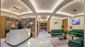A hotel lobby with a reception desk, green sofas, a TV, and a marble floor. - Lords Studio Inn, Jamnagar (Jamnagar)