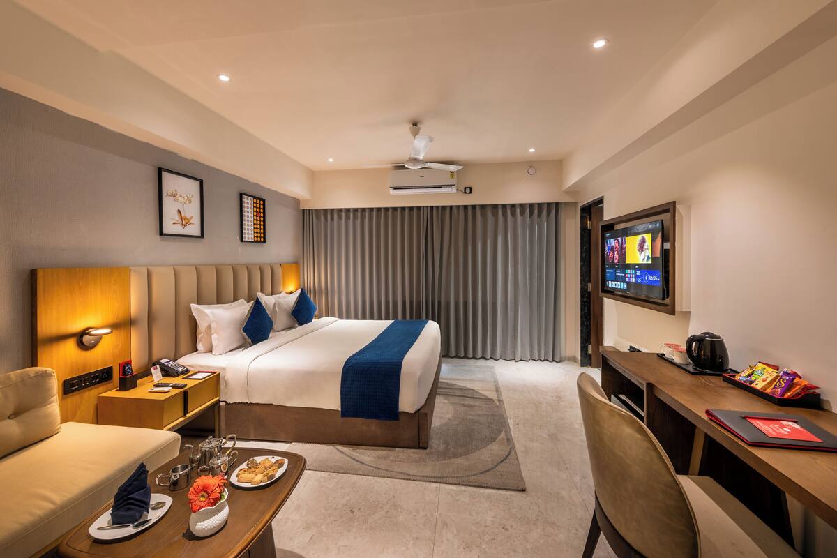 A hotel room with a bed, bedside table, desk, chair, and a television.