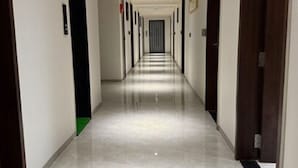 A long, narrow hallway with a shiny, reflective floor and doors on both sides. - Lords Studio Inn, Jamnagar (Jamnagar)