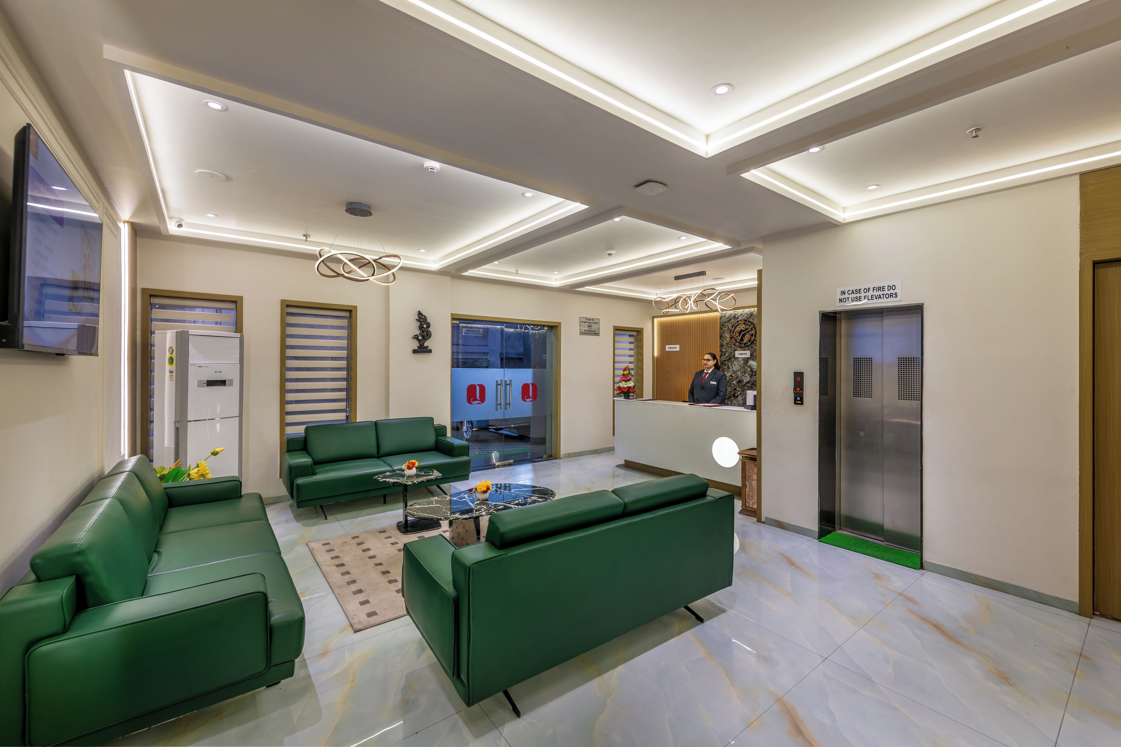 A modern lobby with green sofas, a reception desk, an elevator, and a fire safety sign.