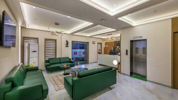 A modern lobby with green sofas, a reception desk, an elevator, and a fire safety sign.