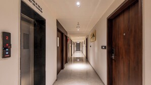A hotel corridor with a digital elevator display, wooden doors, and a long hallway with doors on both sides. - Lords Studio Inn, Jamnagar (Jamnagar)