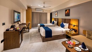 A hotel room with two beds, a desk, a chair, a coffee machine, a TV, and a dining area with plates and cutlery. - Lords Studio Inn, Jamnagar (Jamnagar)