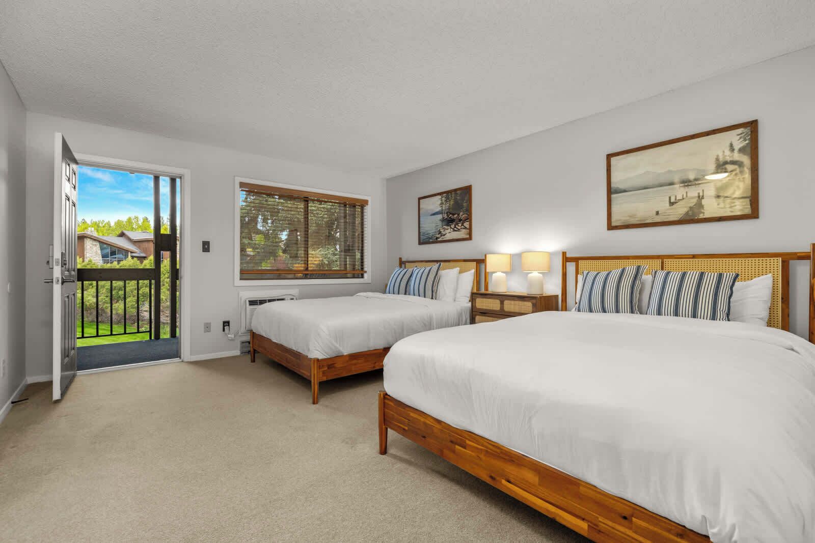 A bedroom with two beds, a door leading to a balcony, and a painting on the wall.