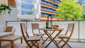 Een balkon met houten meubels, een tafel en stoelen. Er hangt een plant en een lichtslingering.