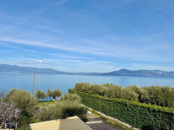 A view of a lake with mountains in the background, surrounded by greenery and a clear sky.