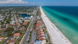 An aerial view of a coastal residential area with a beach, houses, and a clear blue sky.