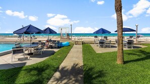 A poolside area with lounge chairs, umbrellas, and a palm tree.