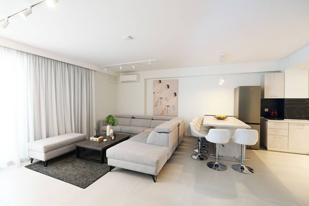 Een moderne woonkamer met een grijze modulaire bank, een salontafel en een eethoek met barkrukken.
