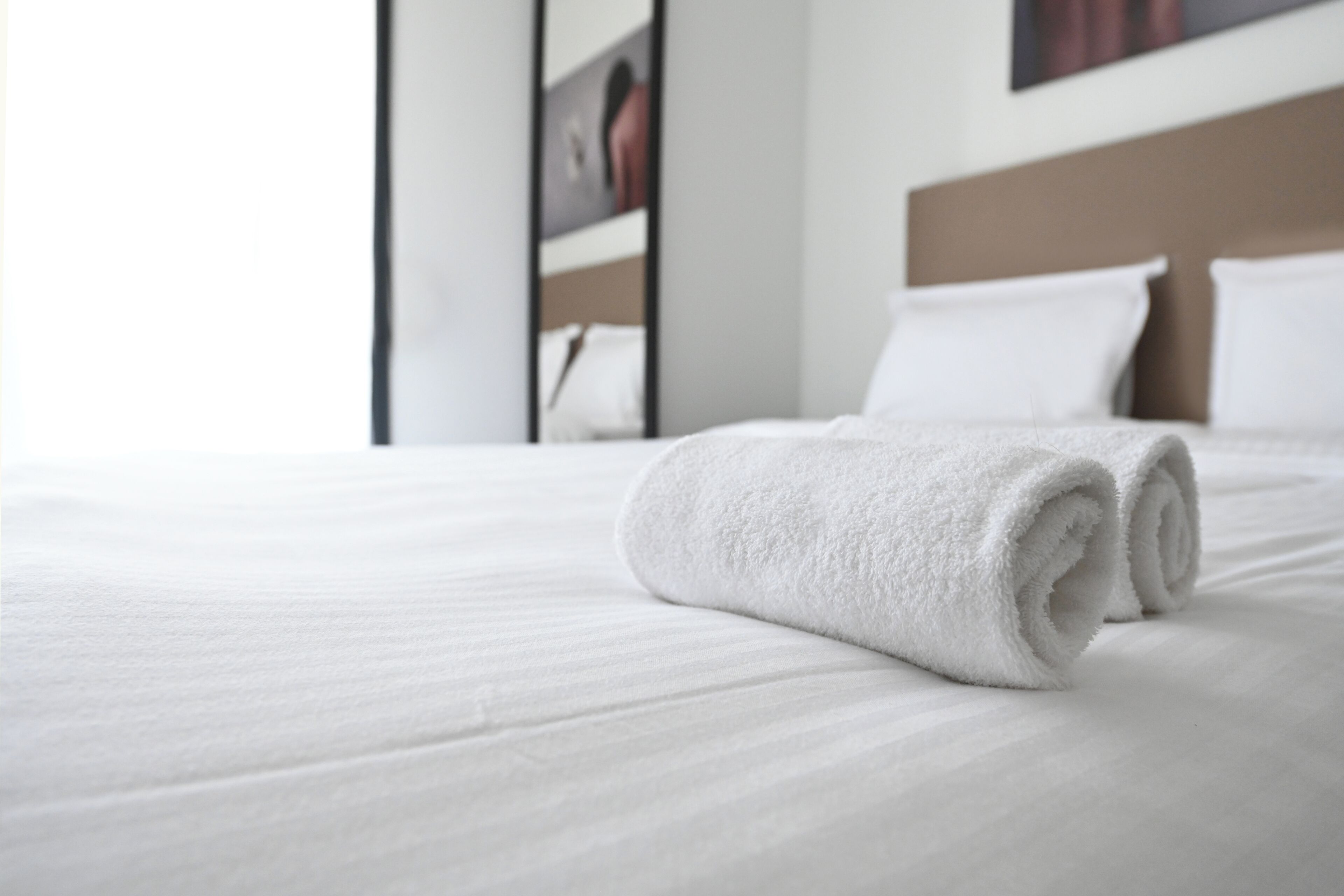 A neatly made bed with white linens and a rolled white towel.