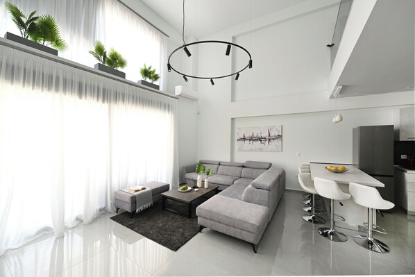 A modern living room with a grey sectional sofa, a coffee table, and a dining area with white bar stools.